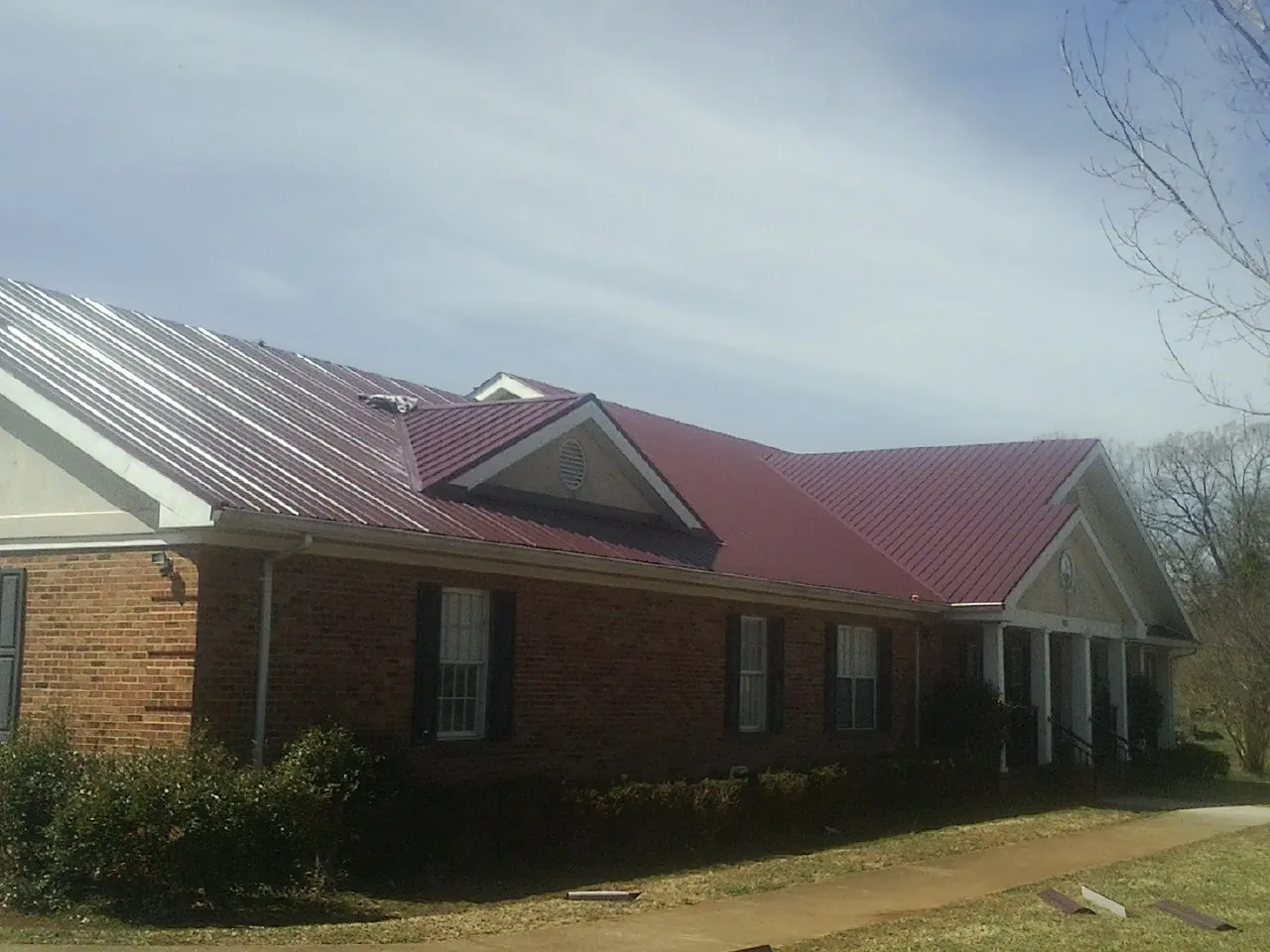 Red metal roof with gabled entries on a long brick building, from a Hail Damage Roof Repair job in Buchanan